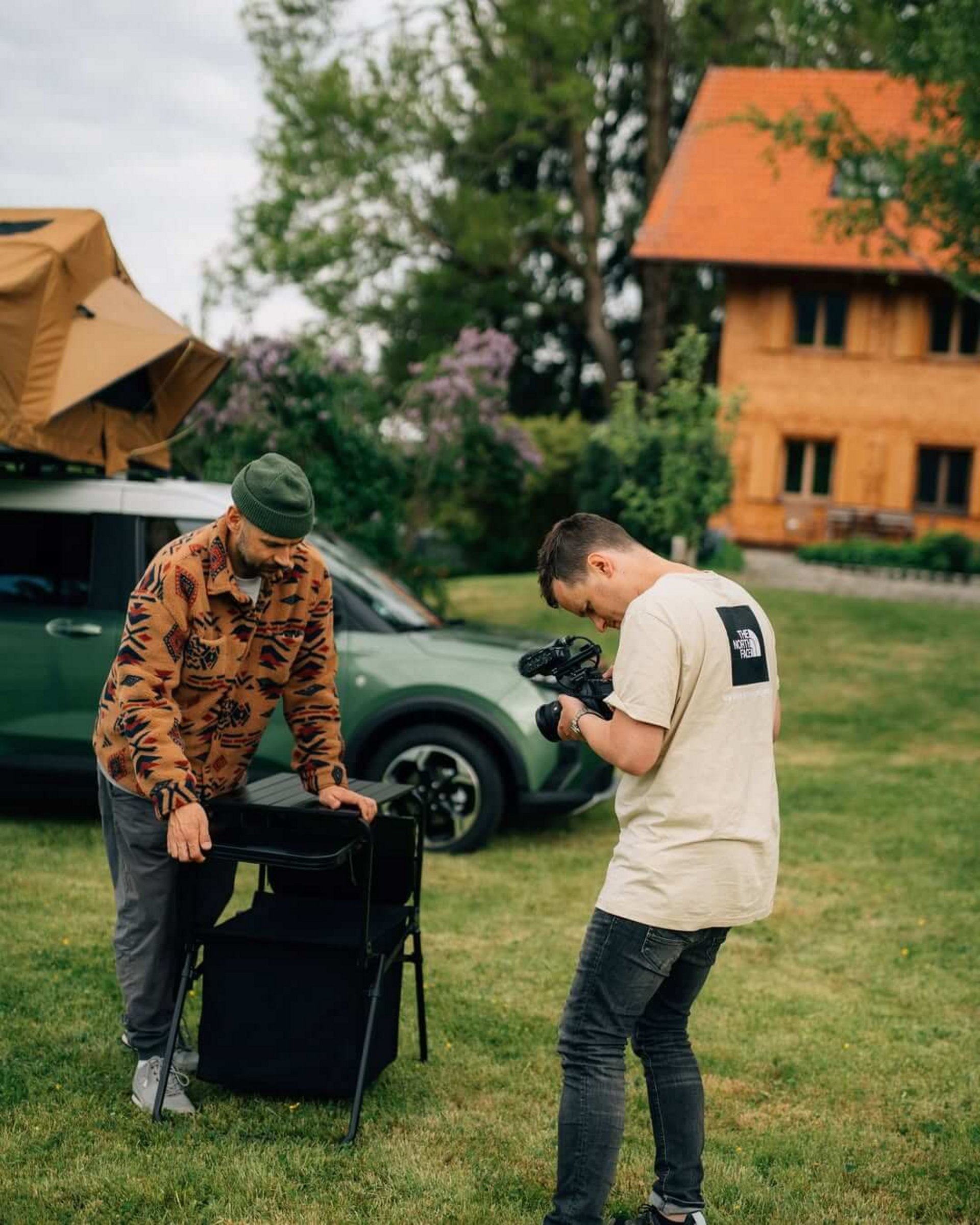 Cameraman filming a man setting up a camping kitchen box next to a van with a roof tent