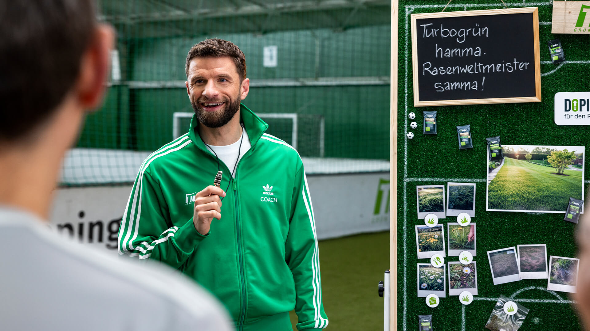 Thomas Müller with a coach's whistle in front of the turbogrün tactics board reading "Turbogrün hamma. Rasenweltmeister samma!"